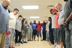 Men huddle to pray at the close of an Overcomers support group meeting